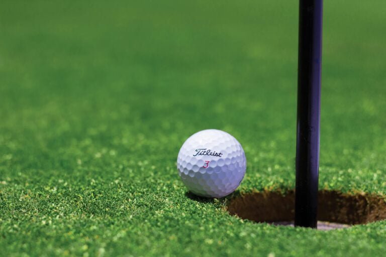Bola de golf a punto de entrar en un hoyo en el que se ve el pado de su bandera.